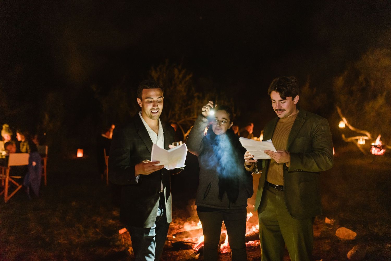 Nighttime outdoor celebration with lanterns and fire pits creating ambient lighting.