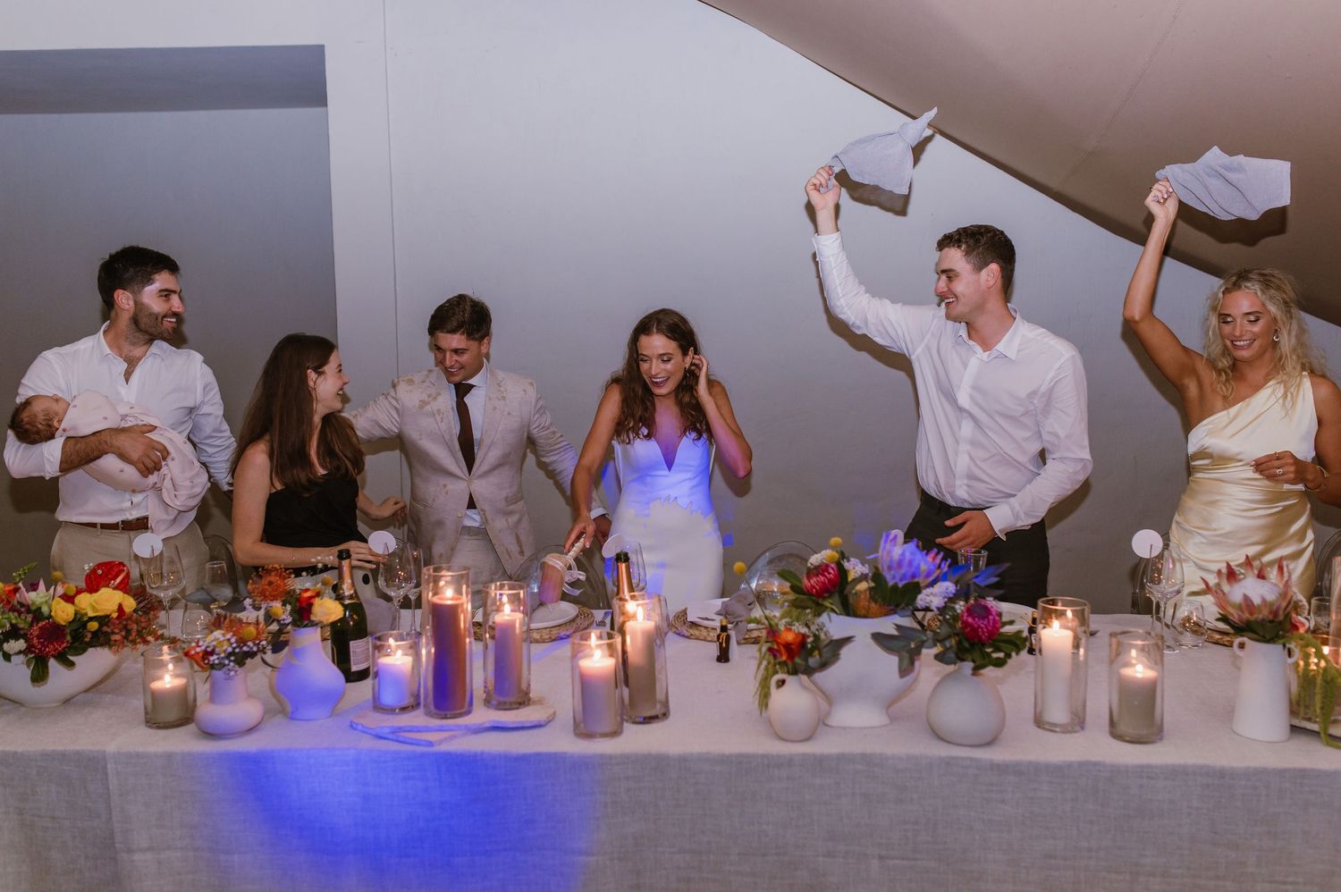 Wedding reception table setting with candles, floral centerpieces and blue accent lighting.