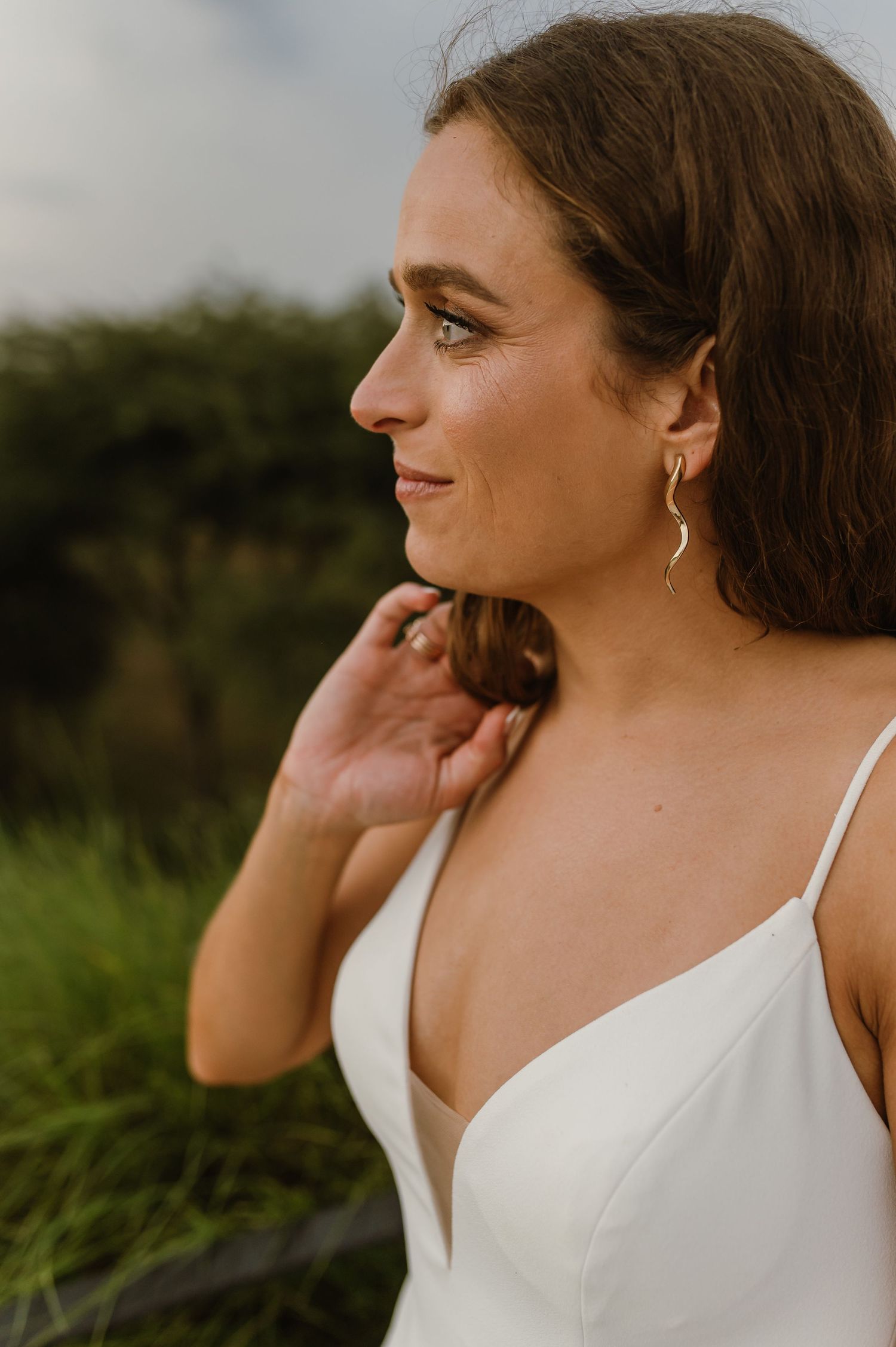 Profile view of bride wearing delicate earrings and v-neck wedding dress.