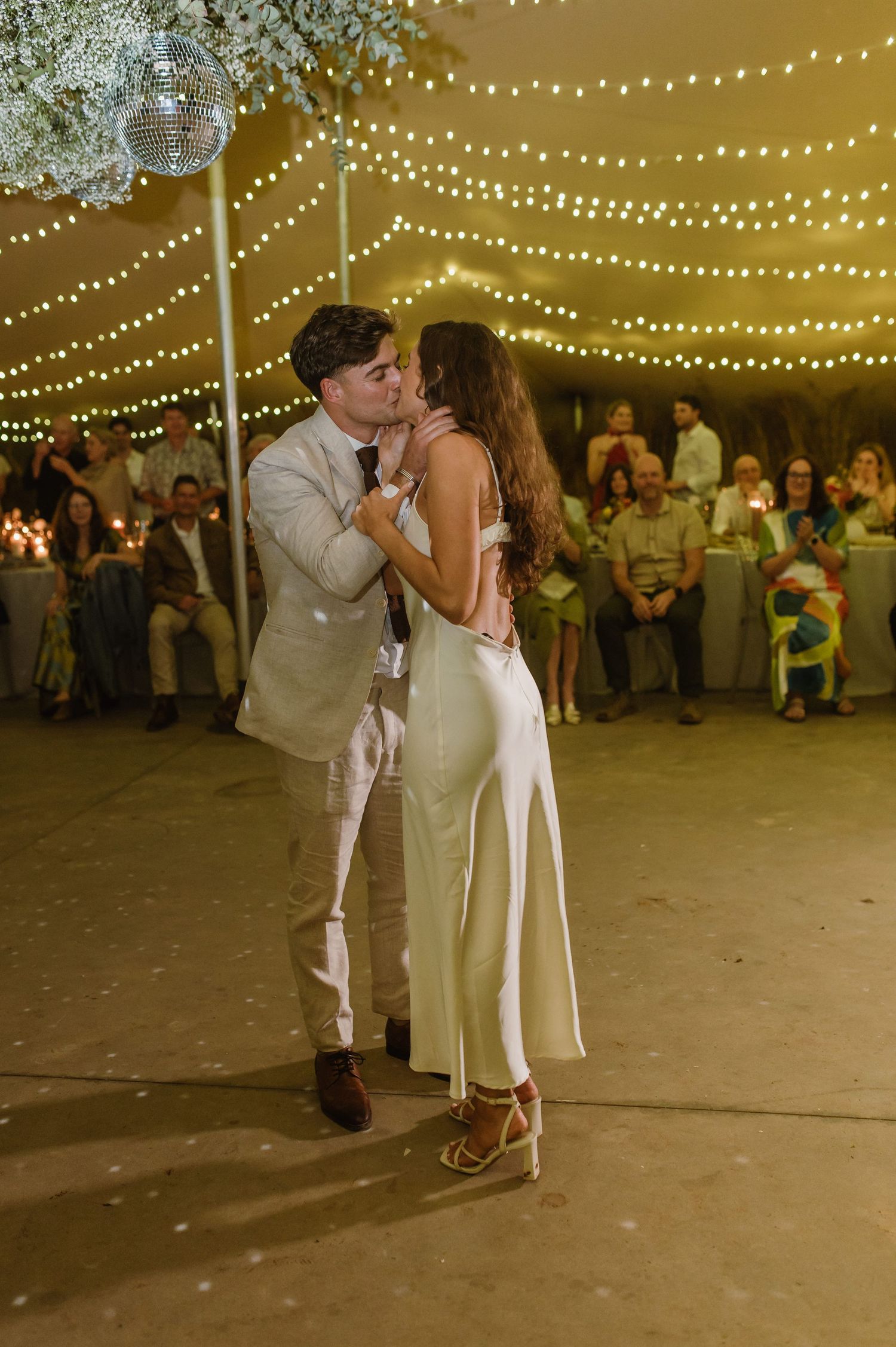 Intimate dance moment between newlyweds under decorative string lights at their reception.