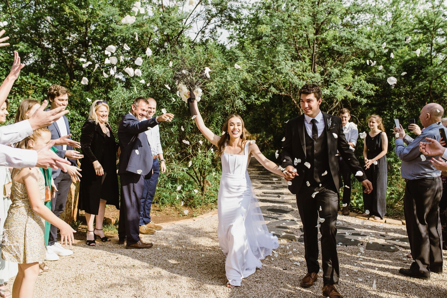 Wedding celebration with guests gathered outdoors under tree canopy.