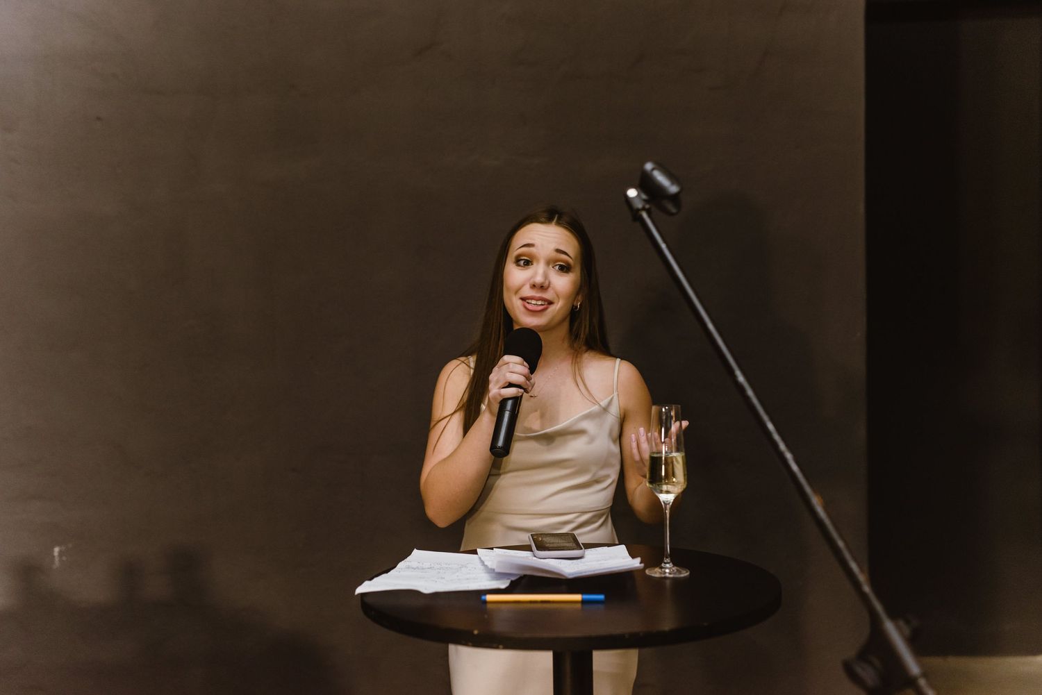 A person in formal attire gives a speech at a wedding reception while holding a microphone.