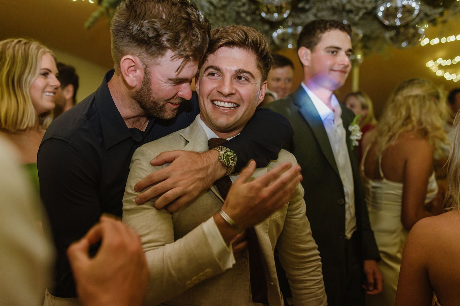 Guests enjoying themselves on a lively dance floor with string lights overhead at a wedding reception.
