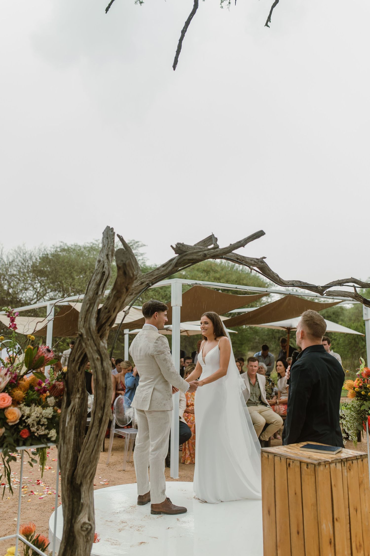 An outdoor wedding ceremony setup with rustic driftwood decor and colorful floral arrangements.