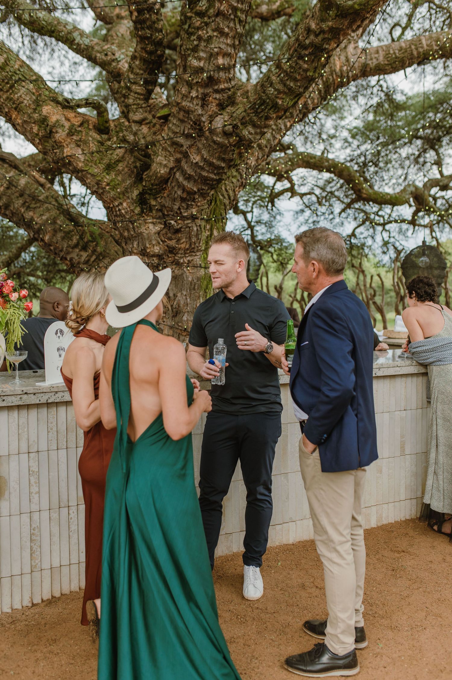 Casual outdoor gathering with guests socializing under string lights and trees.