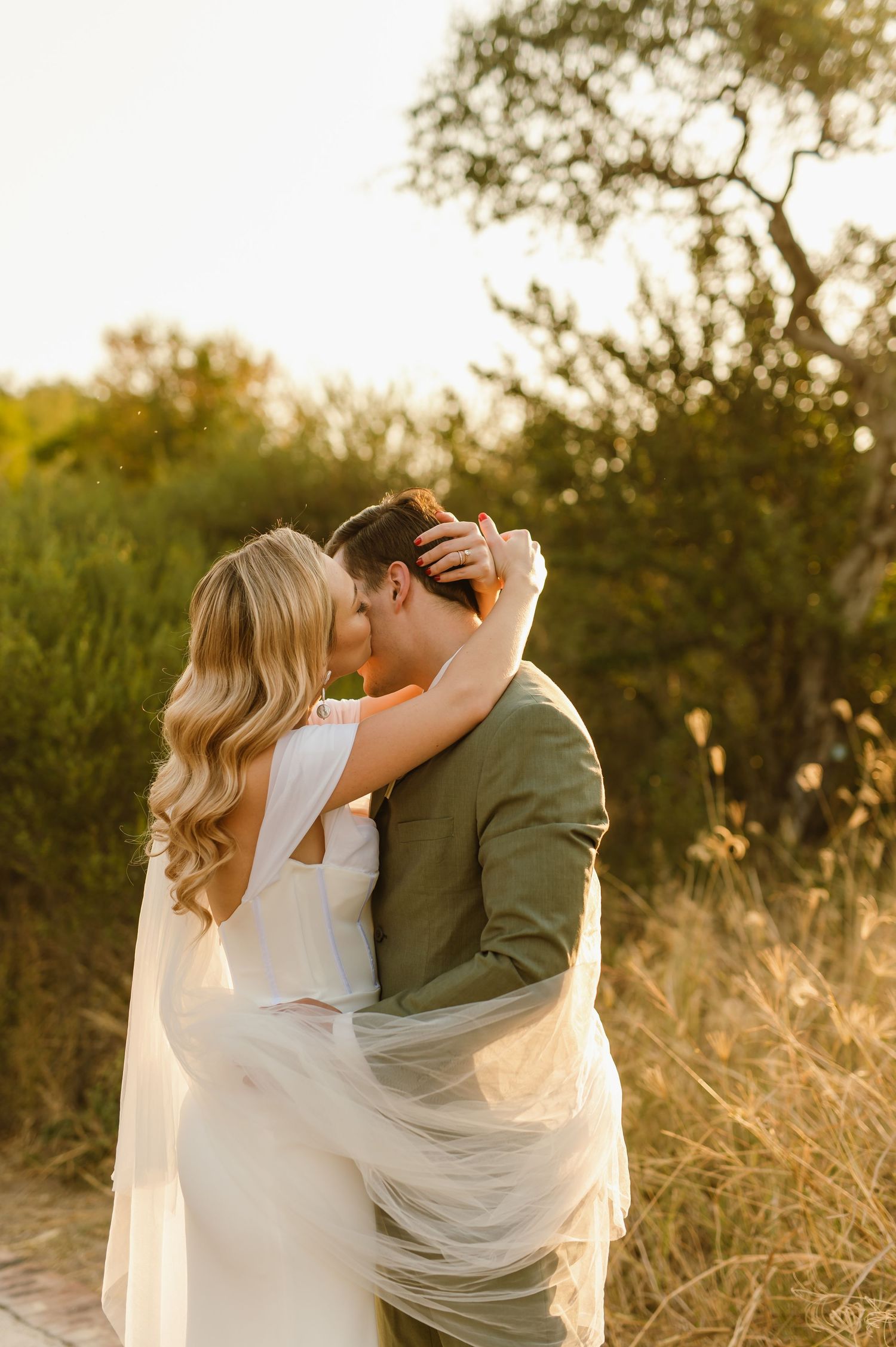 Intimate wedding moment captured with flowing veil against golden sunset light.