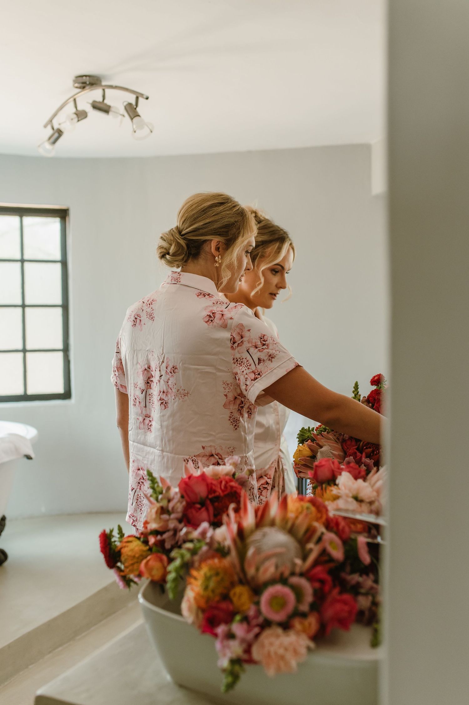 Elegant floral arrangements in white vases with pink and orange blooms in a bright room.