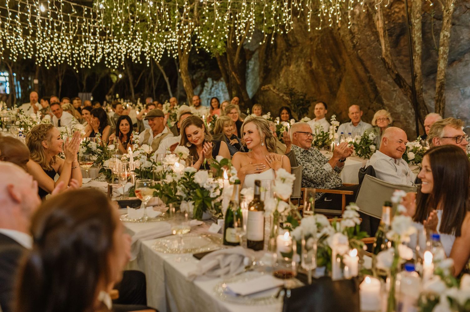 Wedding celebration under twinkling lights with guests seated at elegantly decorated tables.