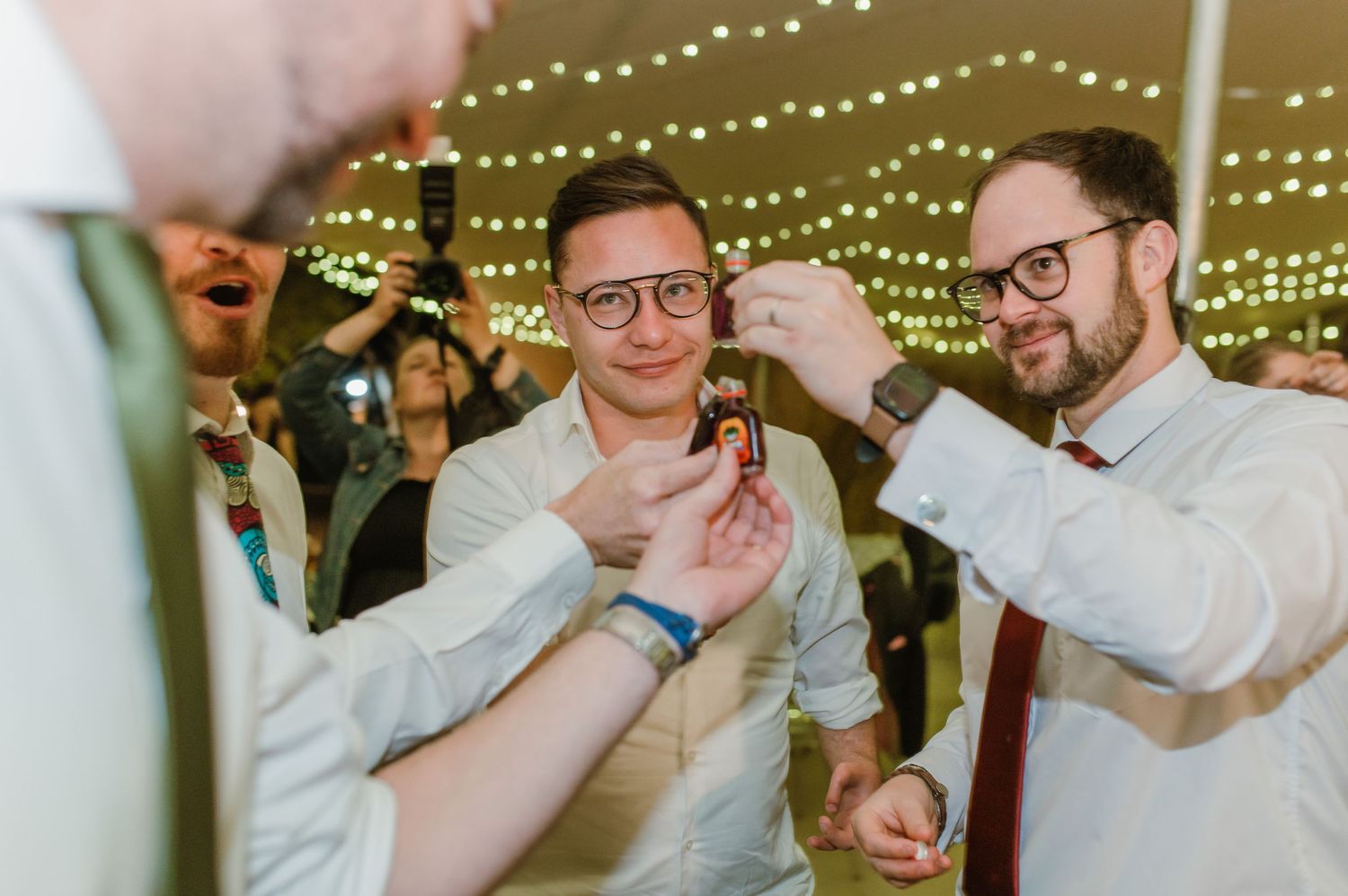 Wedding guests dancing and celebrating under twinkling string lights at a reception party.