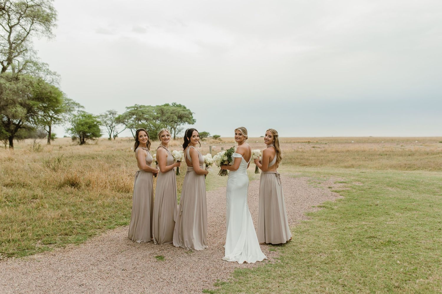 Wedding party in neutral tones posing together in an outdoor natural setting.