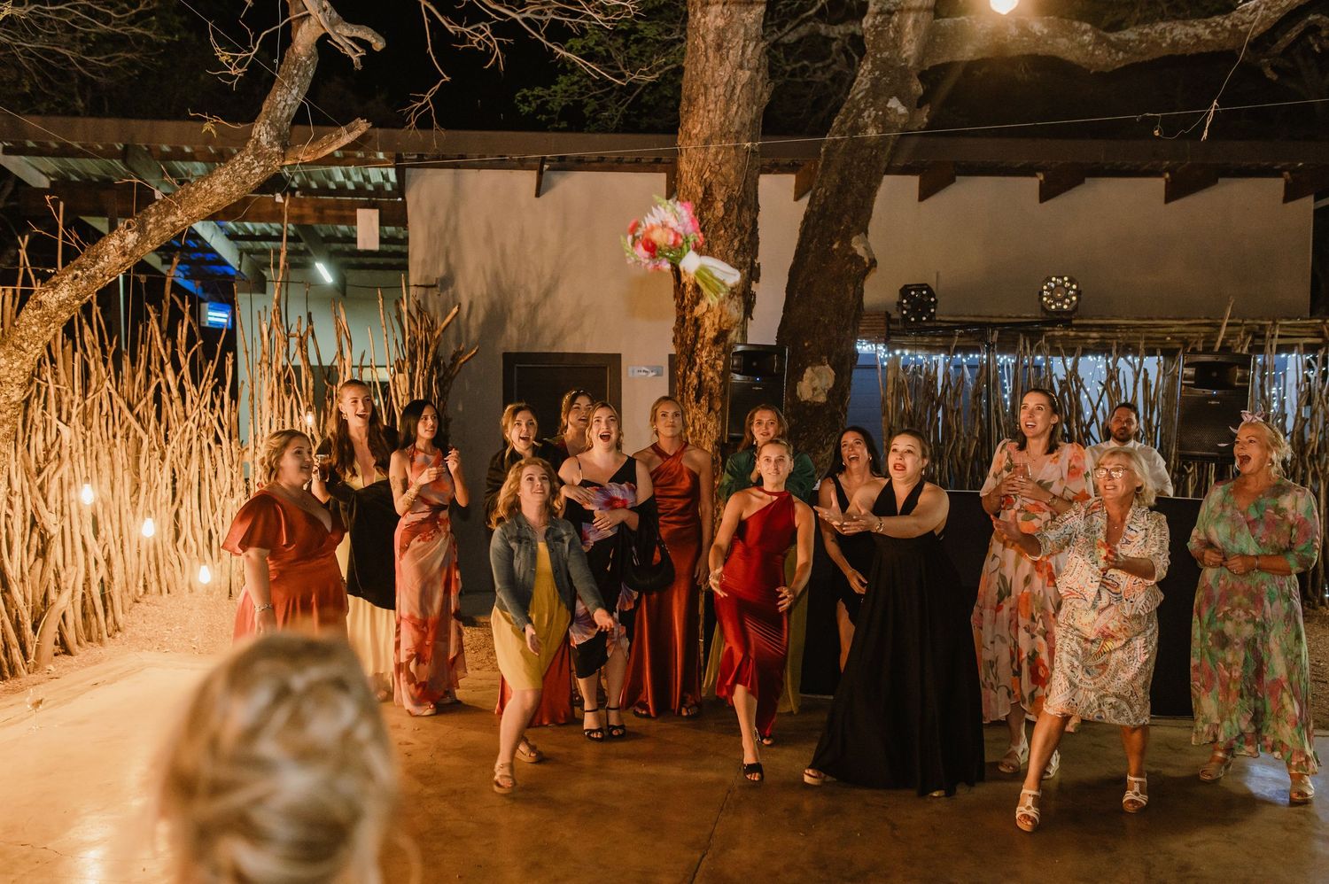 People dancing together at an evening wedding reception in a rustic venue with string lights overhead.