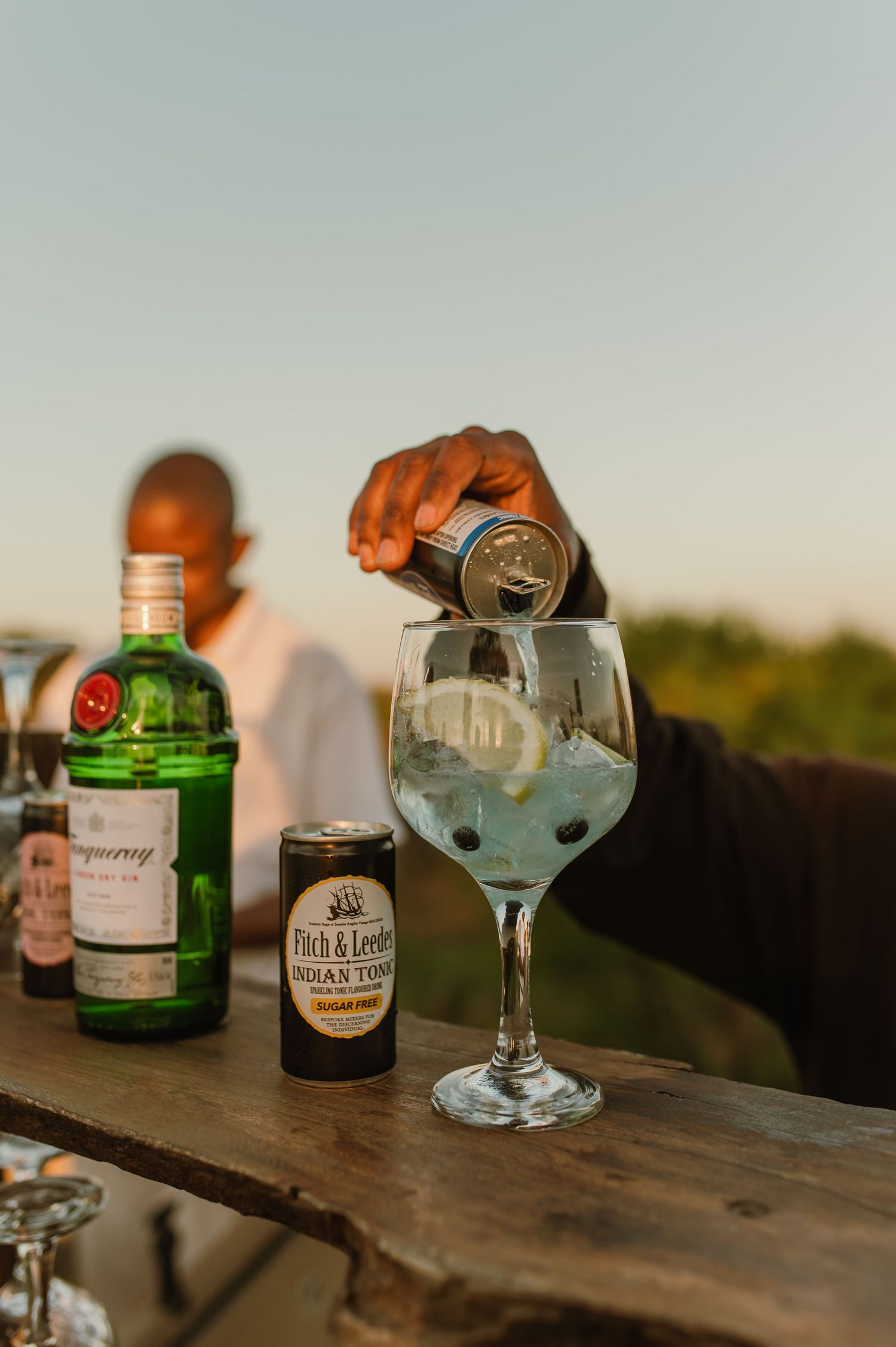 Various liquor bottles and cocktail glasses arranged on a rustic wooden surface at sunset.