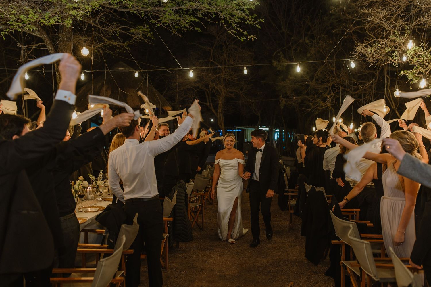 Guests dancing and celebrating at outdoor wedding reception with string lights overhead.