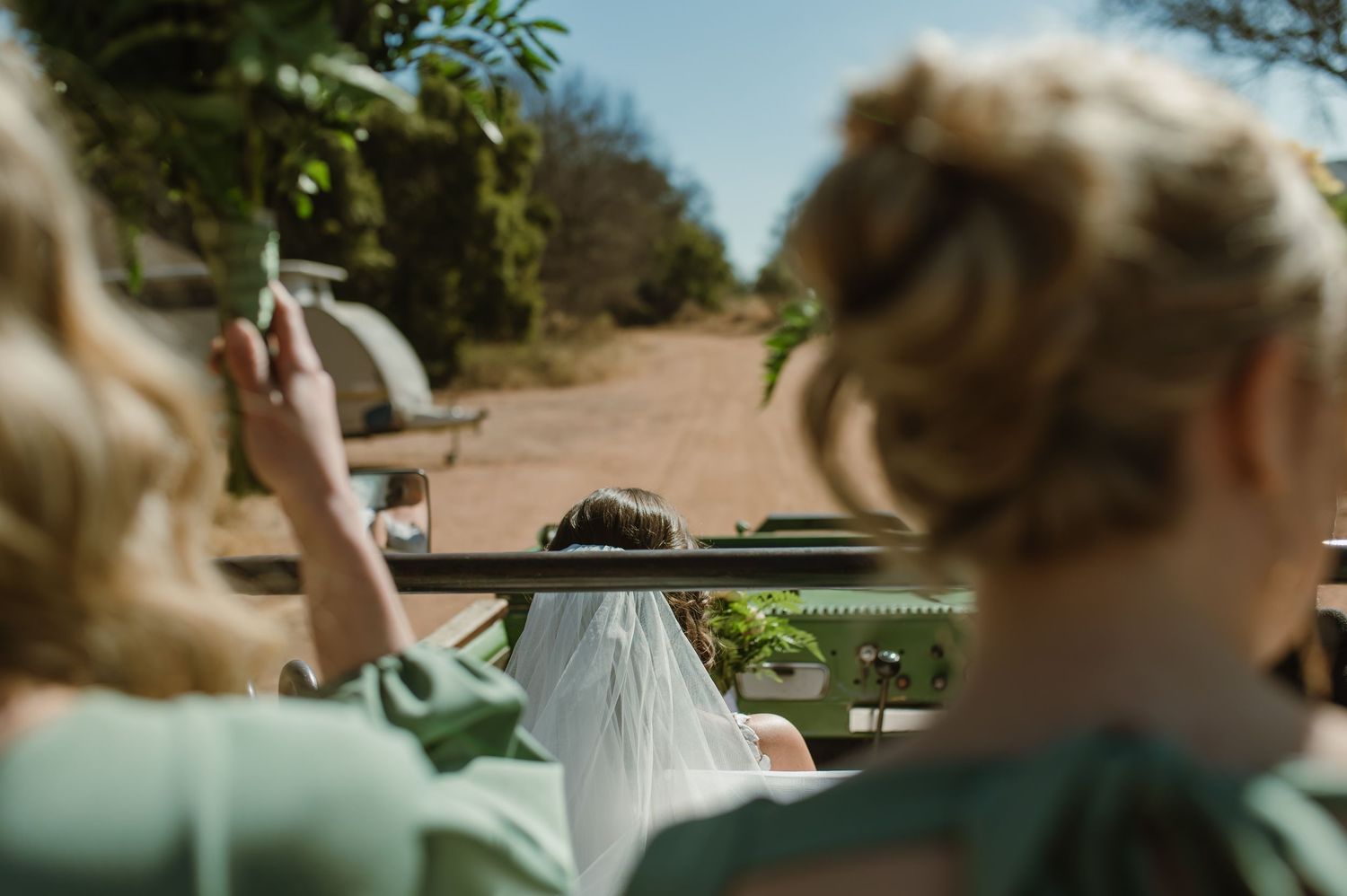 A green safari truck drives along a dusty trail in the wilderness.