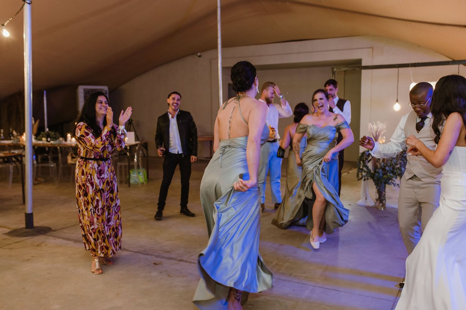 Joyful dancing and celebration at a rustic outdoor tent wedding reception.