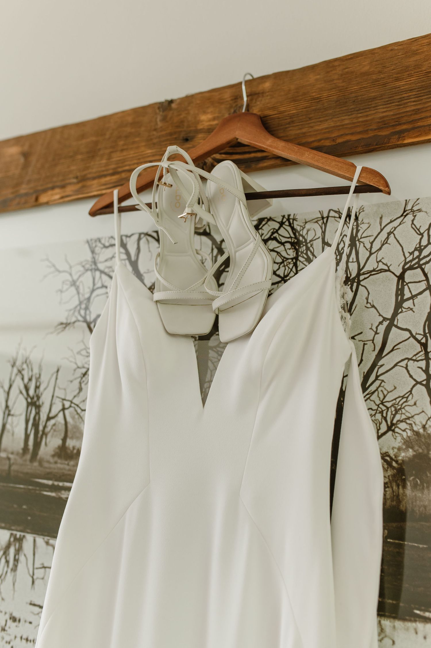 White wedding dresses hanging on wooden hangers against a wall with tree branch wallpaper.