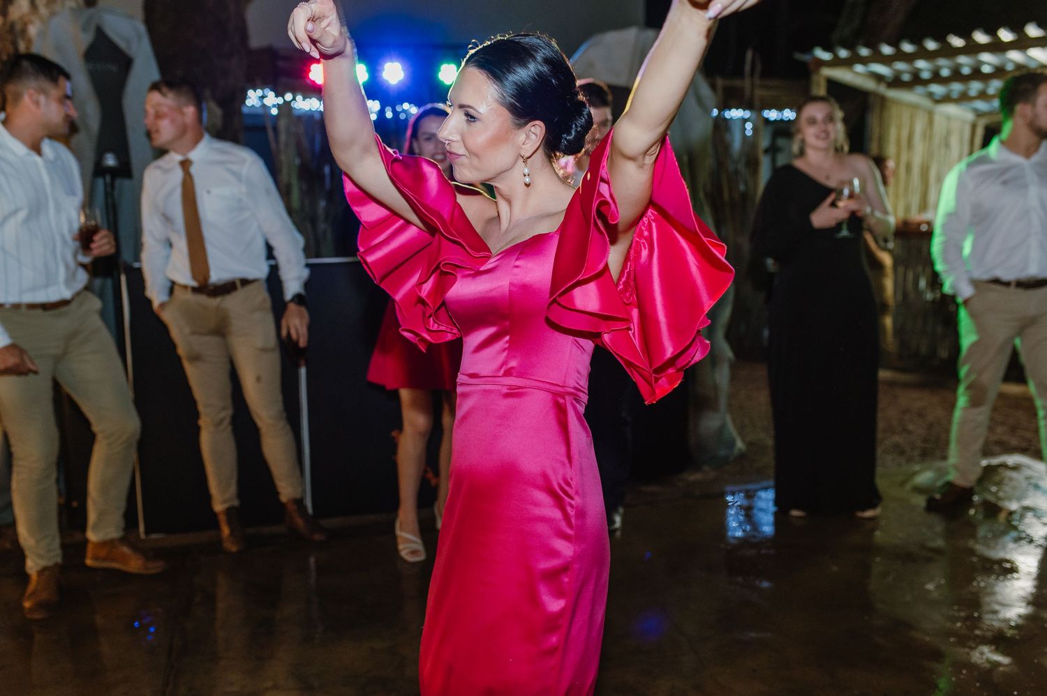 Woman in red satin dress with dramatic sleeves dances joyfully at an evening wedding reception.