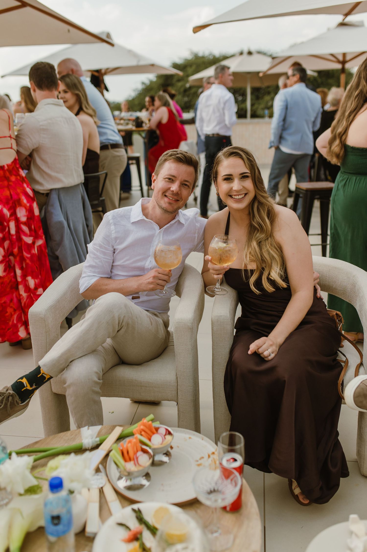 Wedding guests relaxing on white lounge furniture while enjoying cocktails at an outdoor reception.