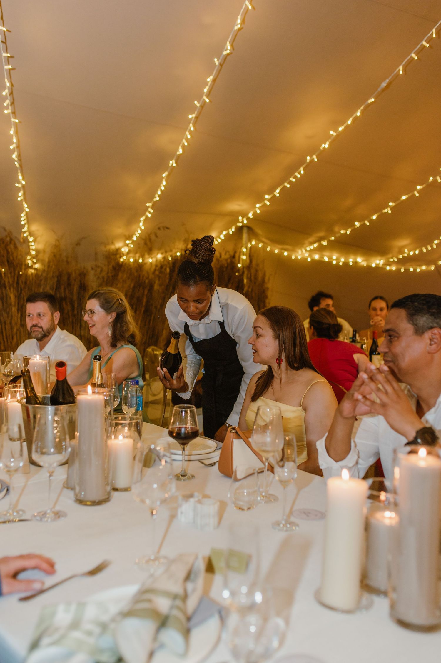 Wedding guests seated at long tables under string lights during an evening reception.