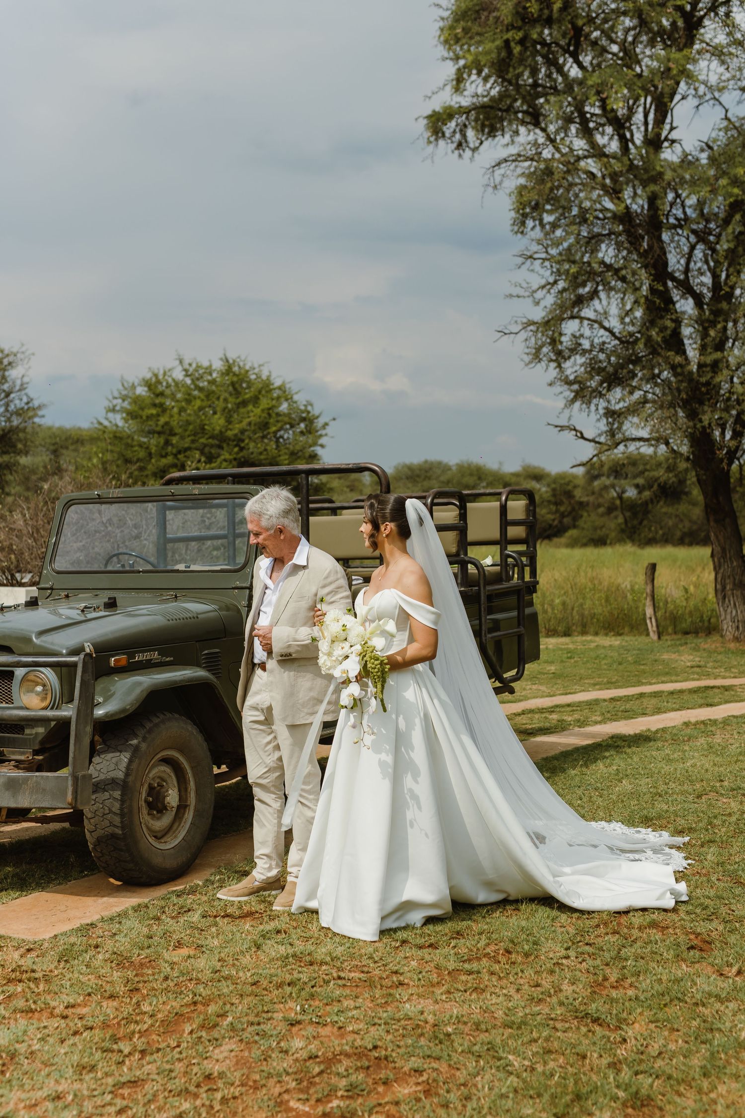 Wedding party gathered near a classic military vehicle on a grassy lawn.