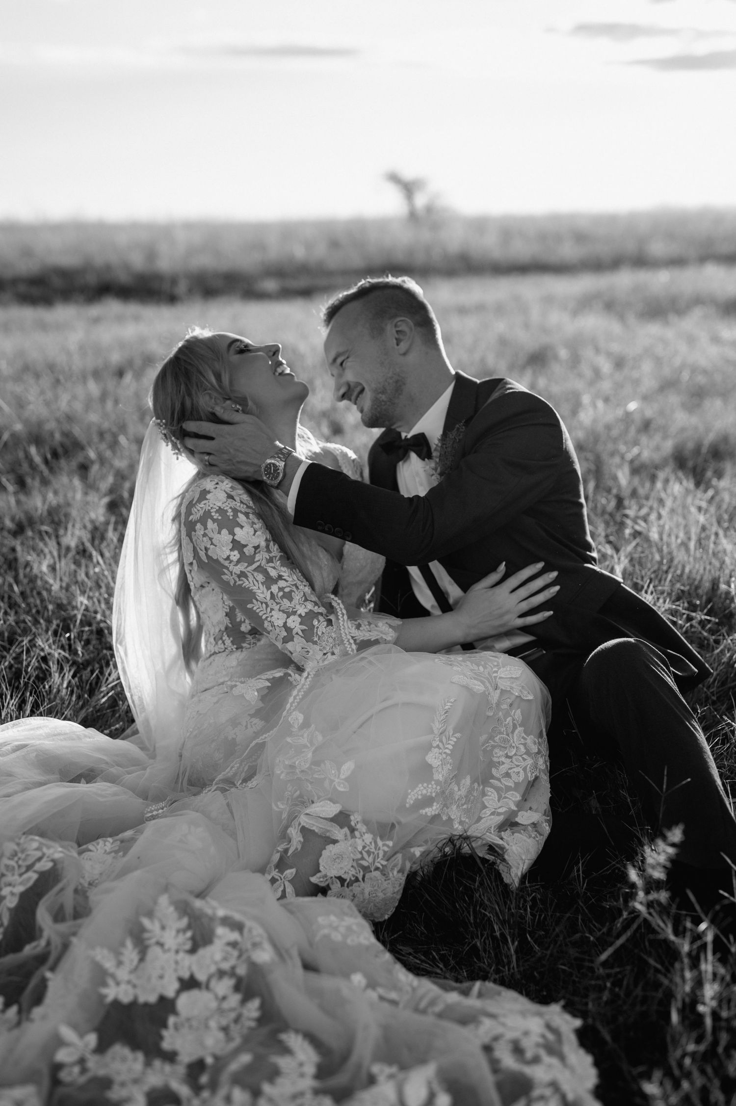 Romantic black and white portrait of newlyweds embracing in tall grass.