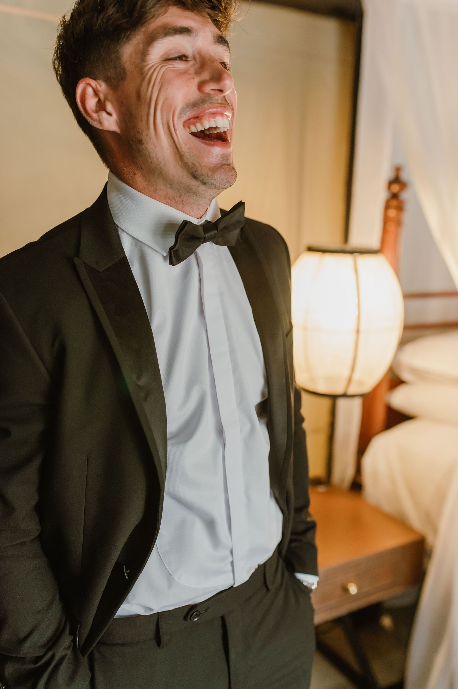 Candid moment capturing genuine laughter in a formal tuxedo against warm interior lighting.