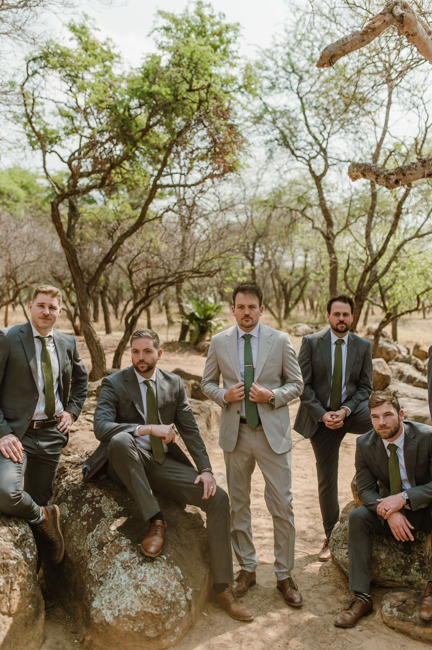 Groomsmen sitting casually on large rocks in a natural outdoor setting.