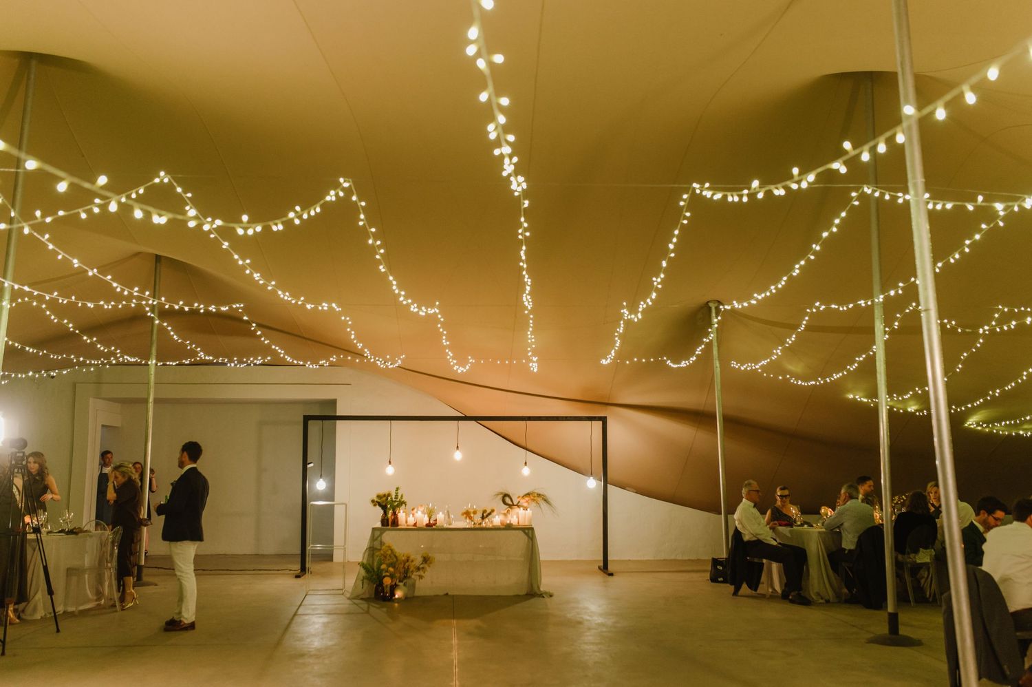 String lights create a romantic canopy over an outdoor wedding reception space.