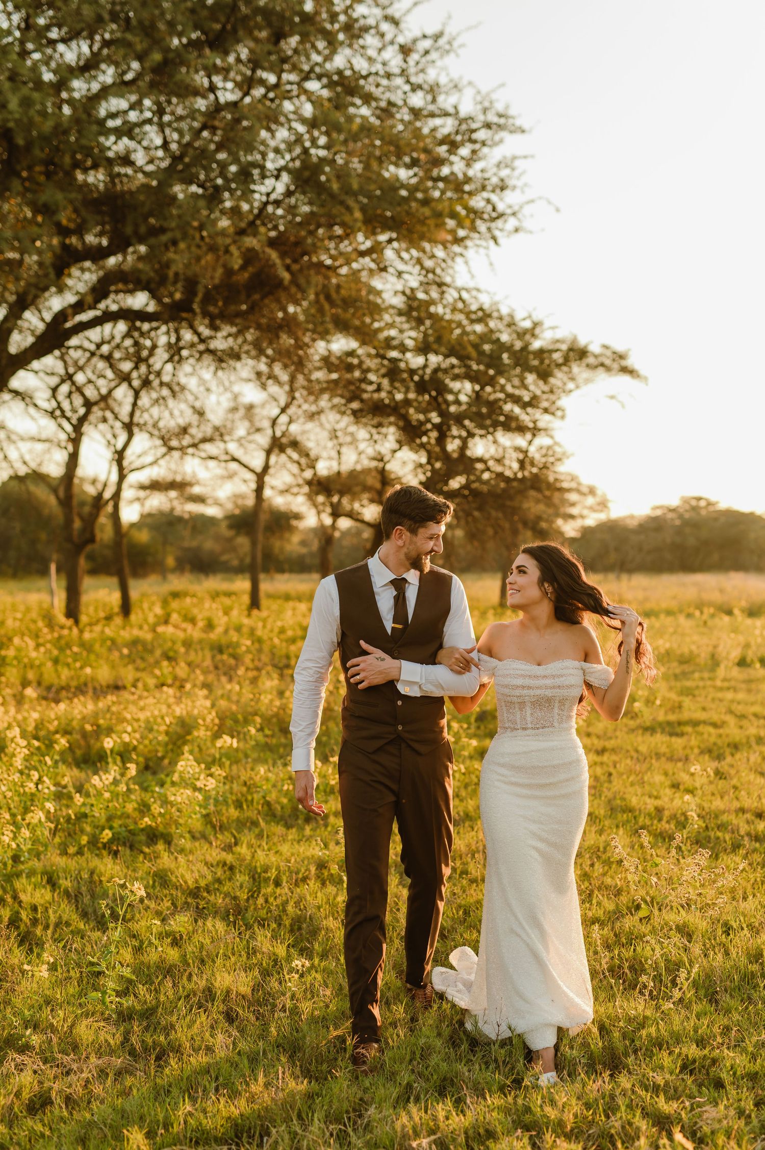 A couple walks hand in hand through a sun-drenched field during golden hour.