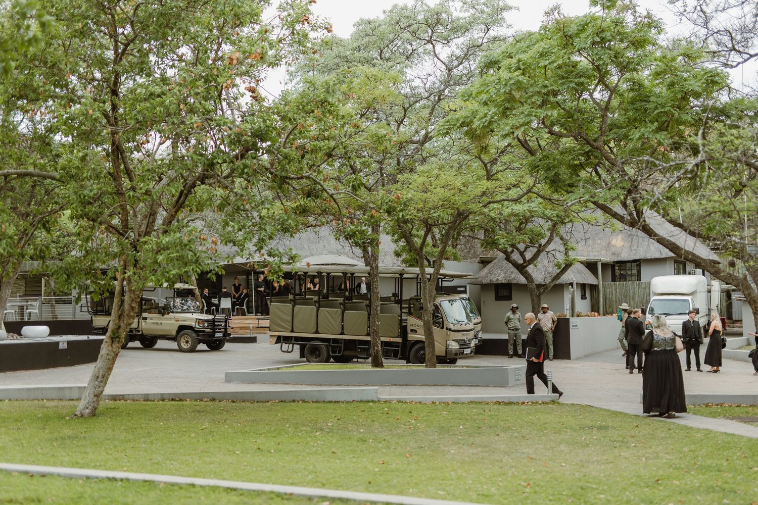 Safari vehicles and guests gathered at an outdoor wedding venue with trees.