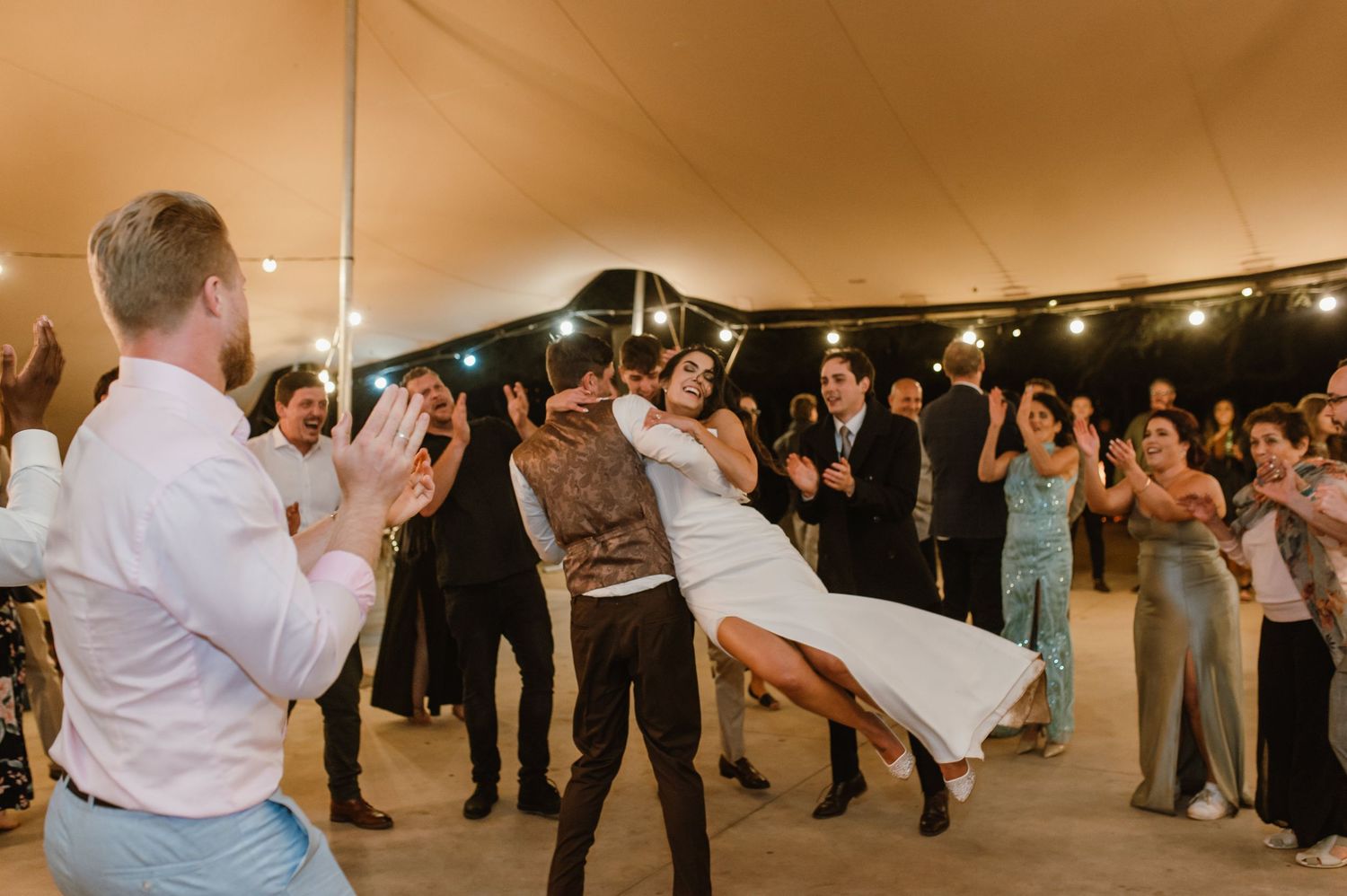 Wedding guests perform dramatic dance moves during a lively reception under string lights.