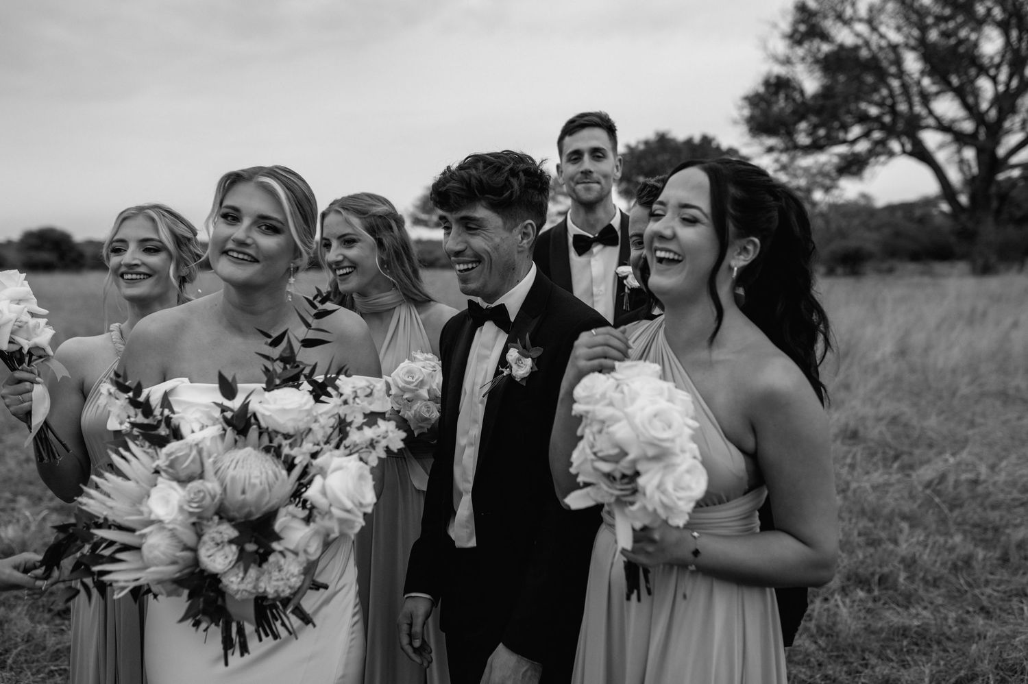 Black and white photo of wedding party celebrating in a natural outdoor setting.