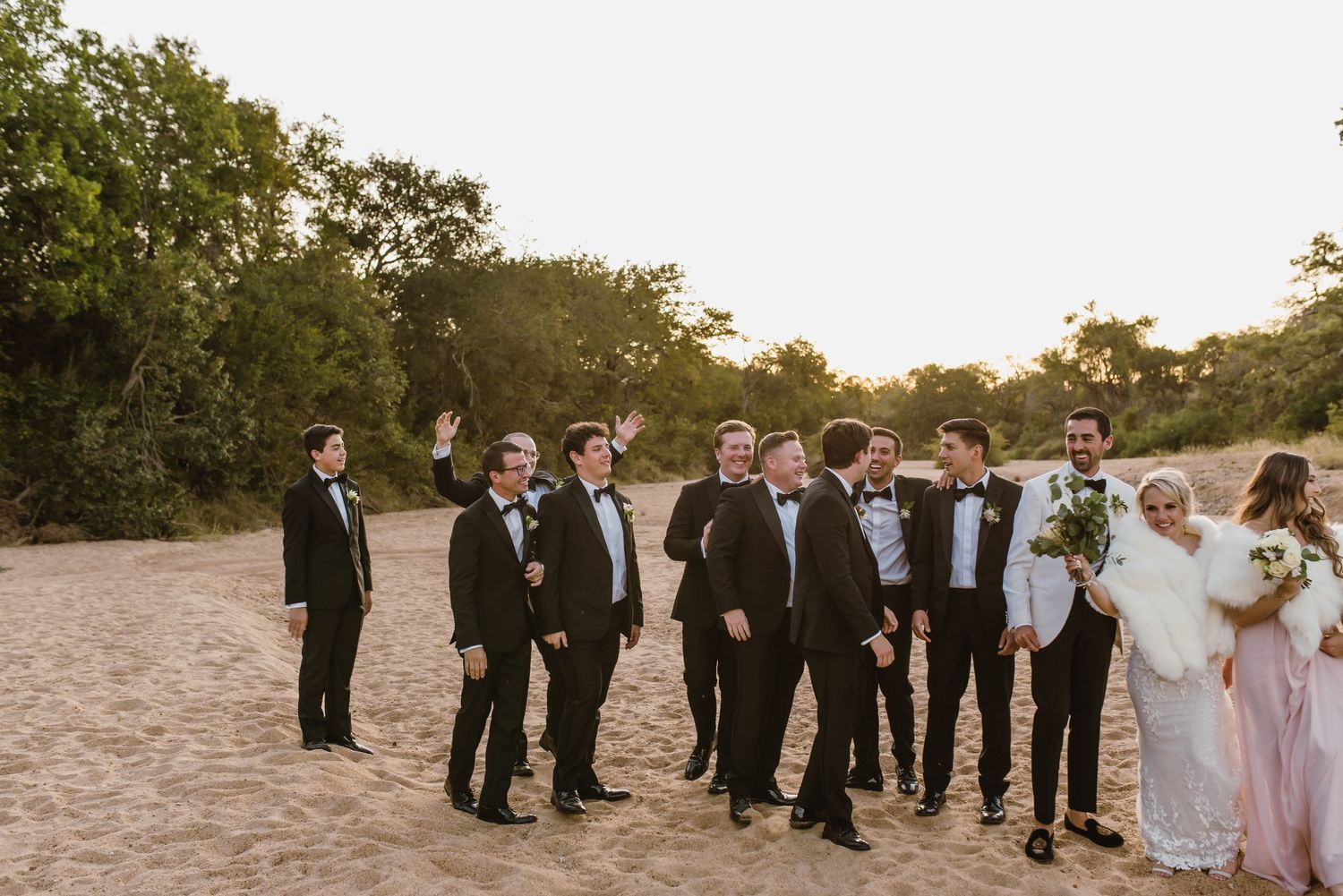 Wedding party arranged in casual poses along sandy beach during golden hour.