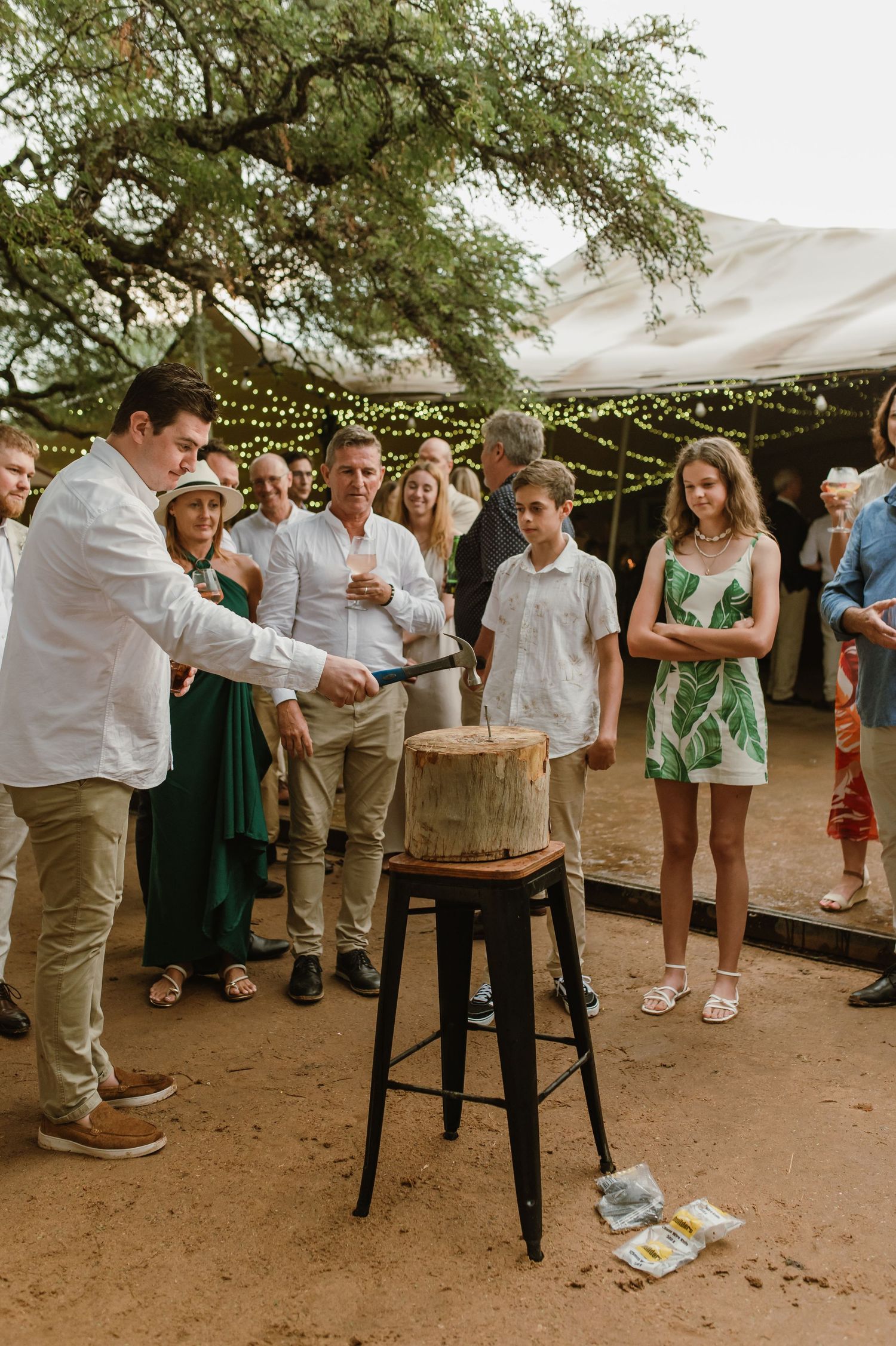 Wedding guests gather around tables under trees for outdoor games and entertainment.