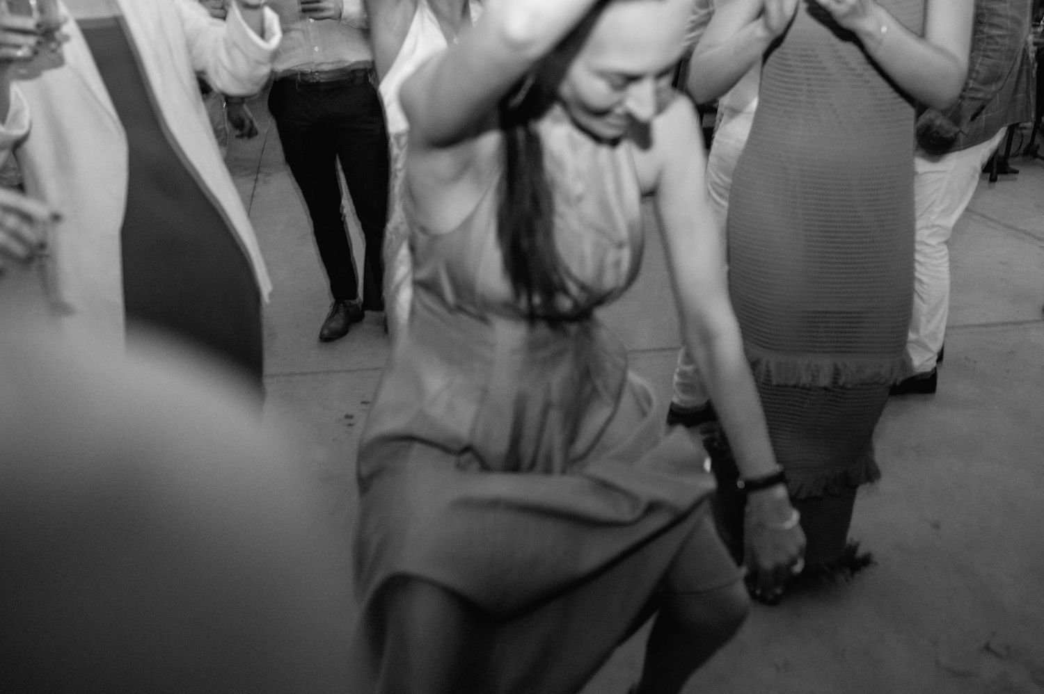 Black and white photo of wedding guests dancing energetically at a lively reception.