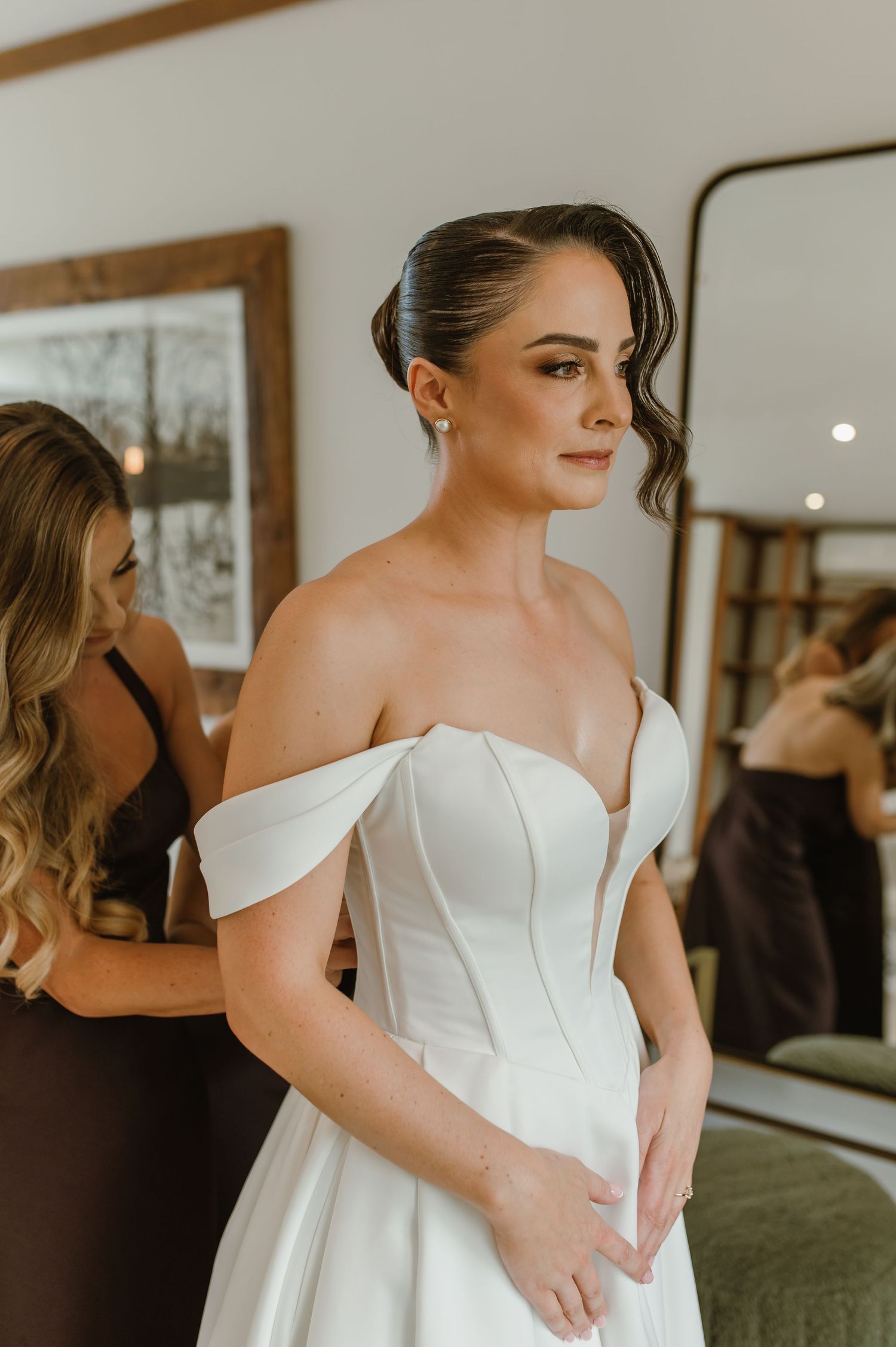 An elegant white wedding gown with off-shoulder detail being fitted in a bridal suite.