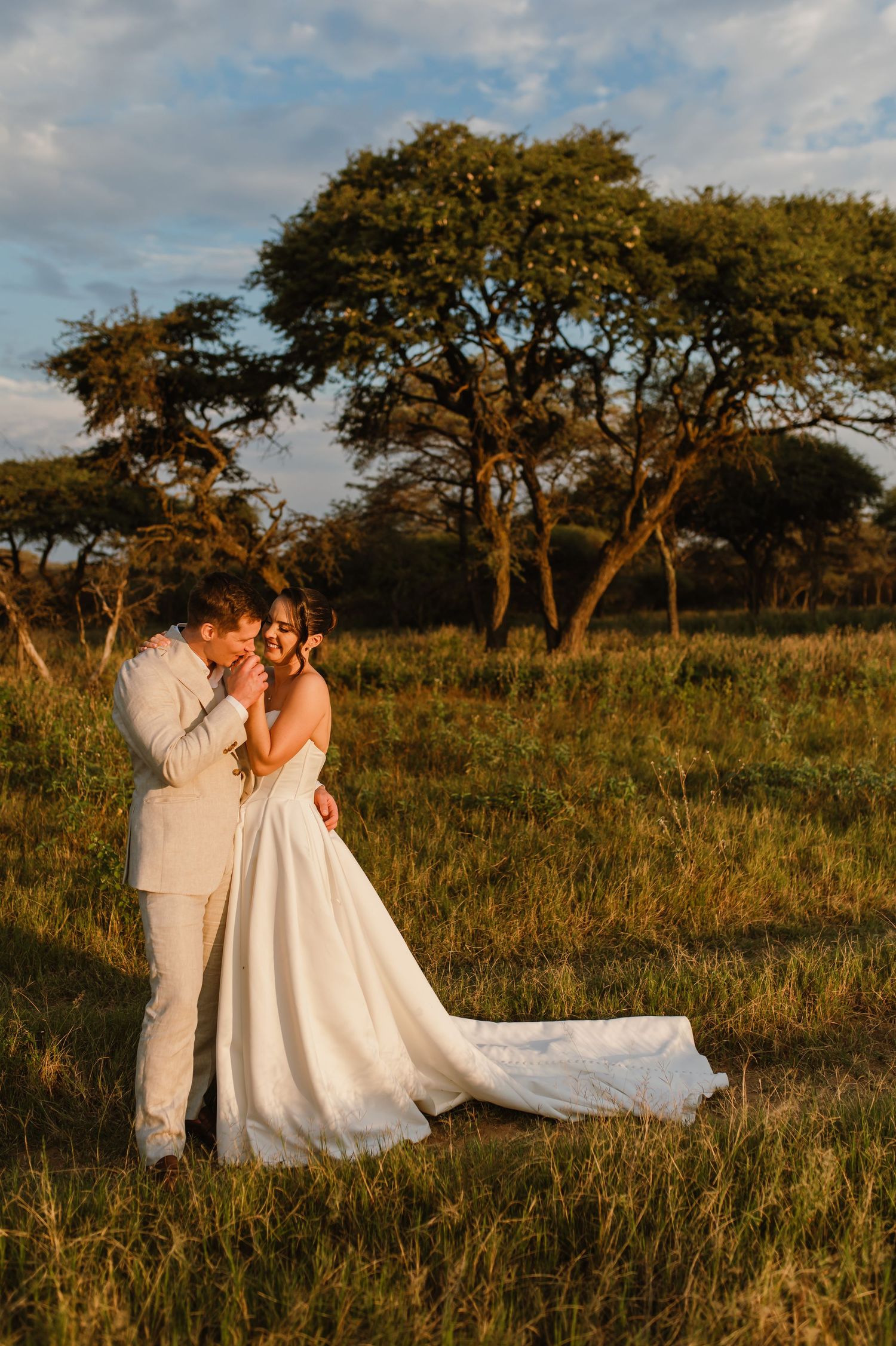 A romantic wedding photo shoot in a golden field at sunset with trees in the background.