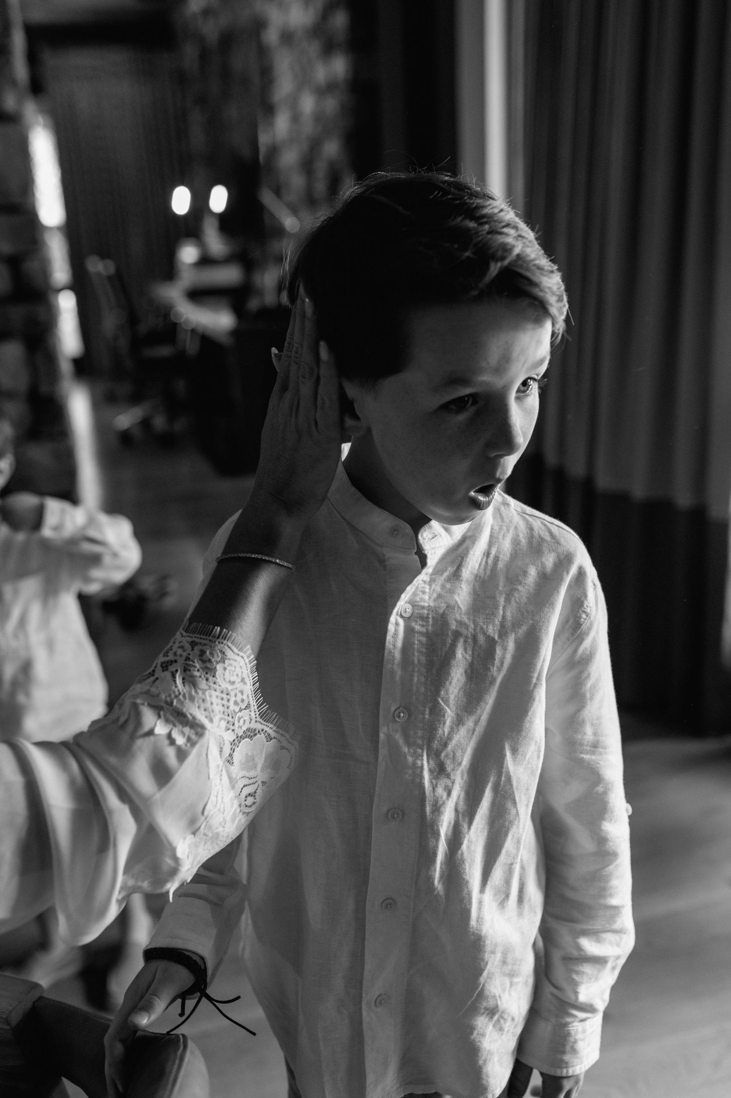 Black and white photo of a boy in a white linen shirt being groomed for a special occasion.