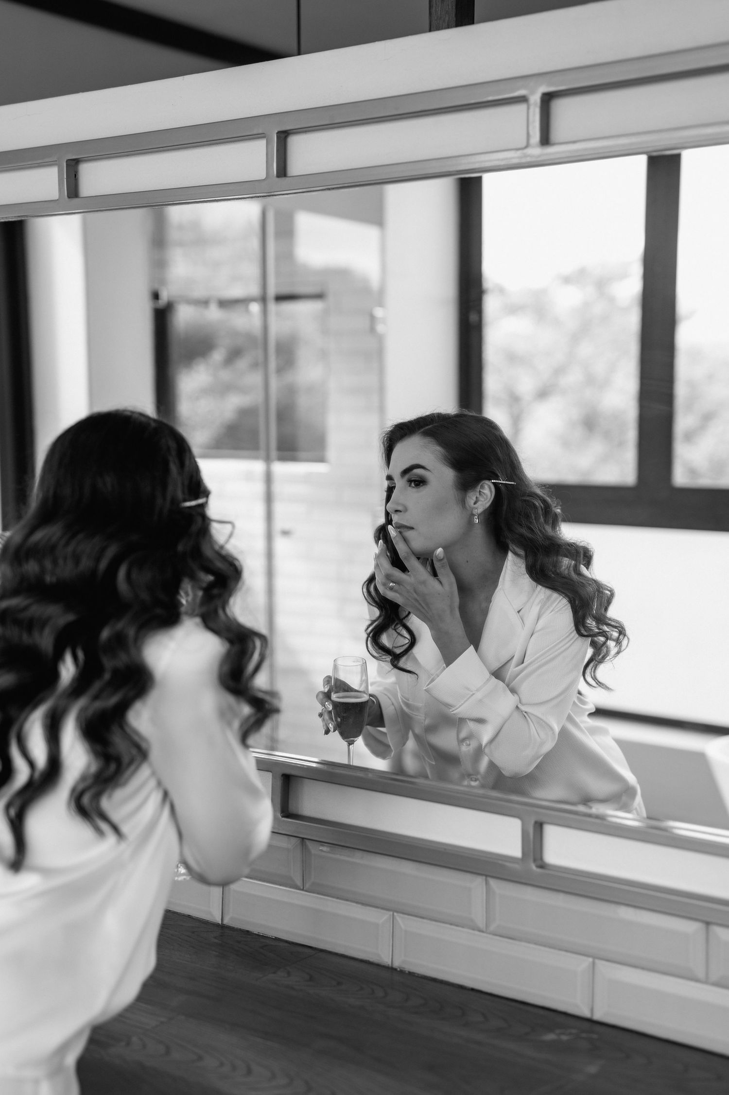Black and white photo of someone applying makeup in a mirror.