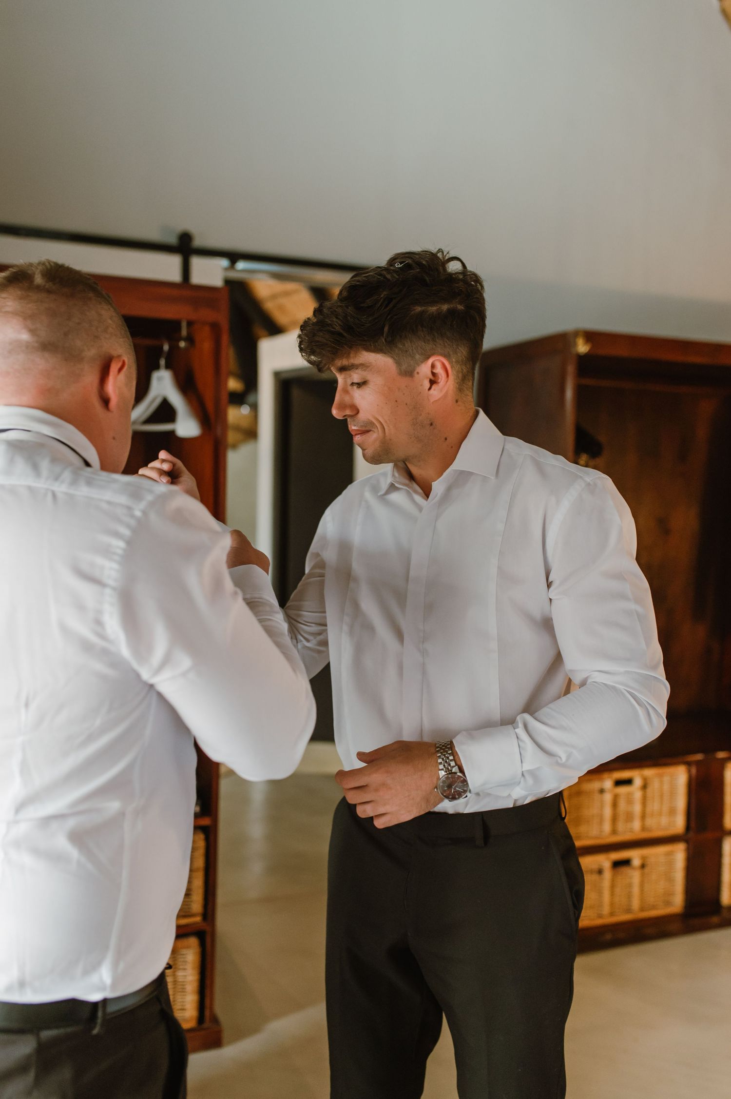 People in white dress shirts helping each other prepare formal attire.