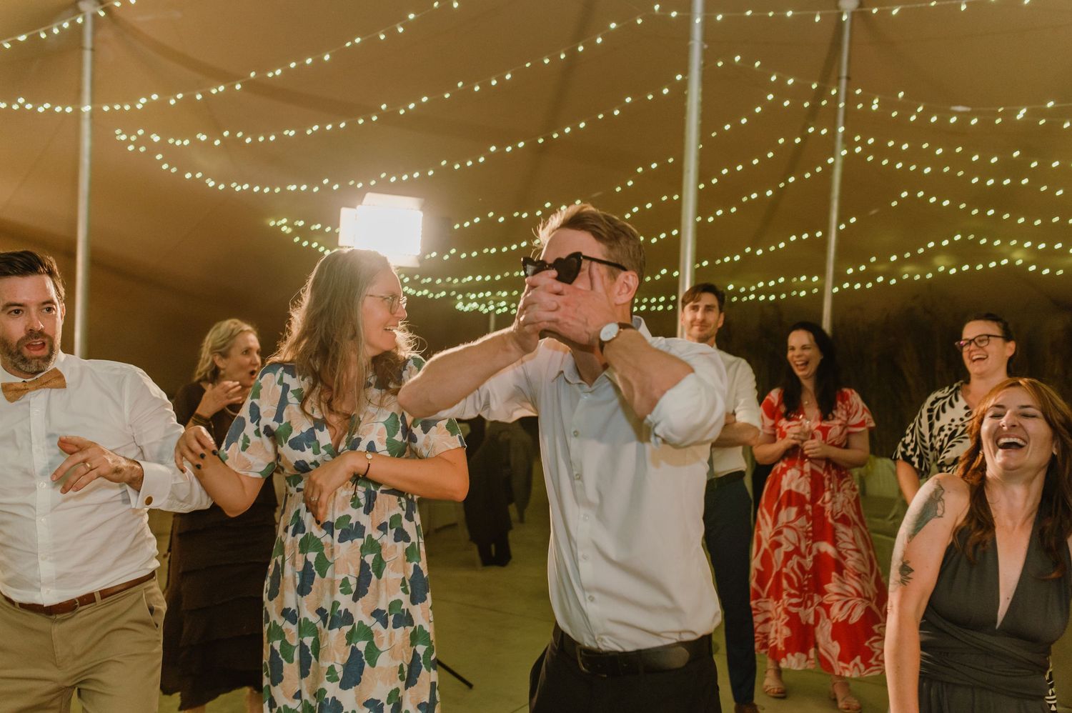 Joyful celebration with guests dancing beneath glowing string lights at a reception.