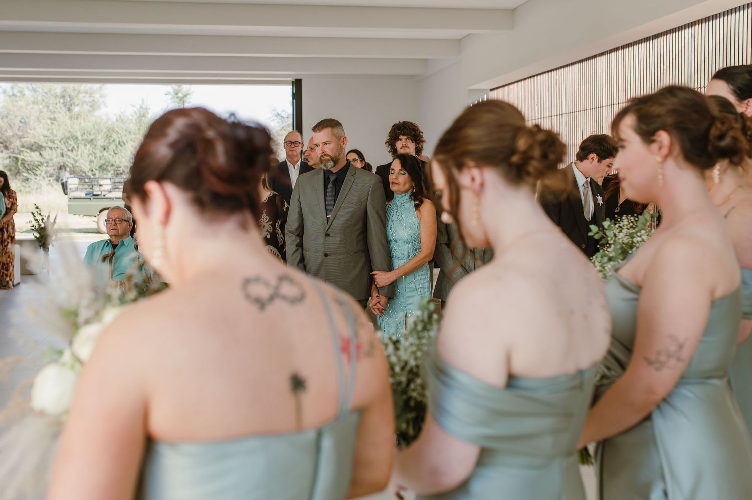 Row of bridesmaids in matching sage green dresses stand together during a wedding ceremony.