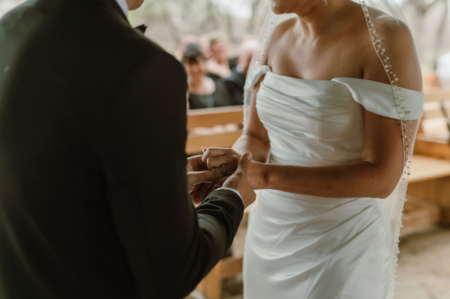 Elegant outdoor wedding scene with off-shoulder white gown against natural backdrop.