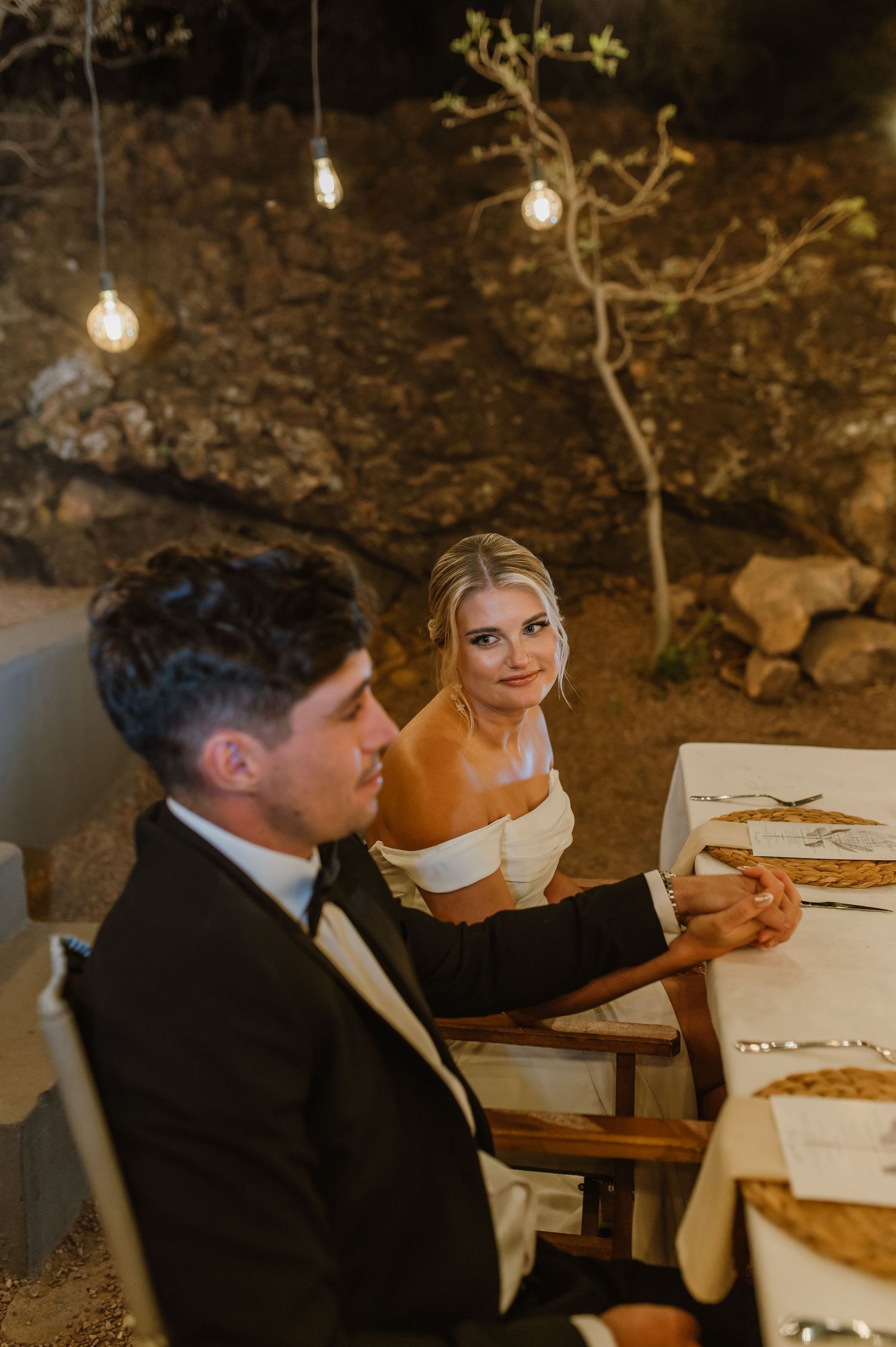 Wedding guests seated at an elegant outdoor dining table with string lights overhead.