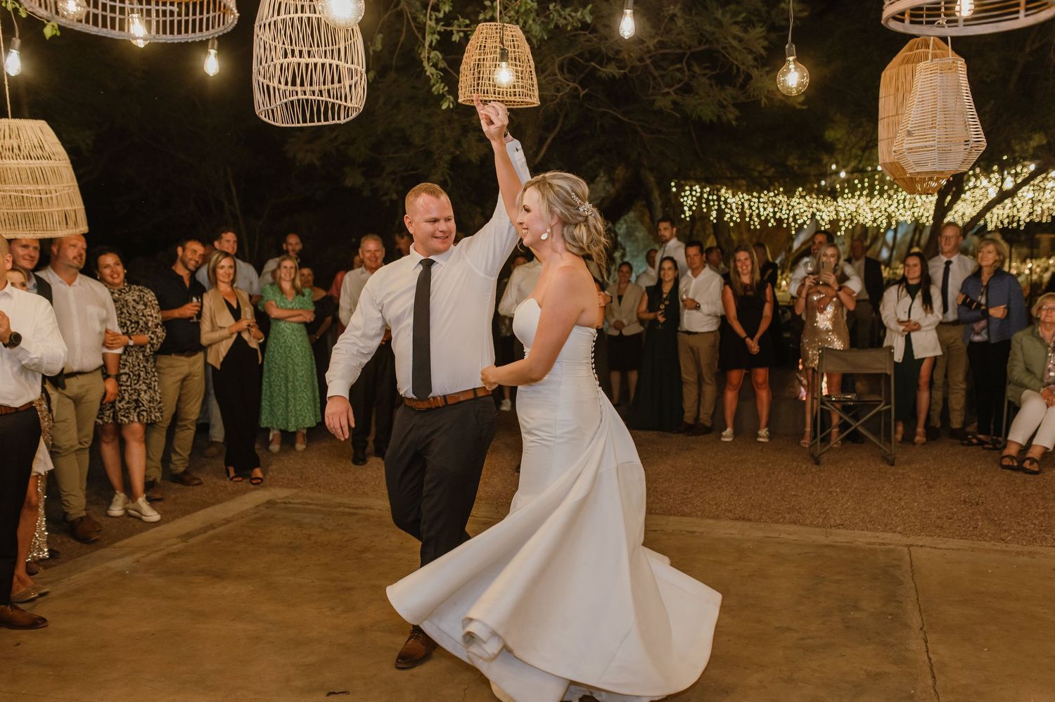 Wedding couple spins on outdoor dance floor decorated with bohemian lanterns and warm lighting.
