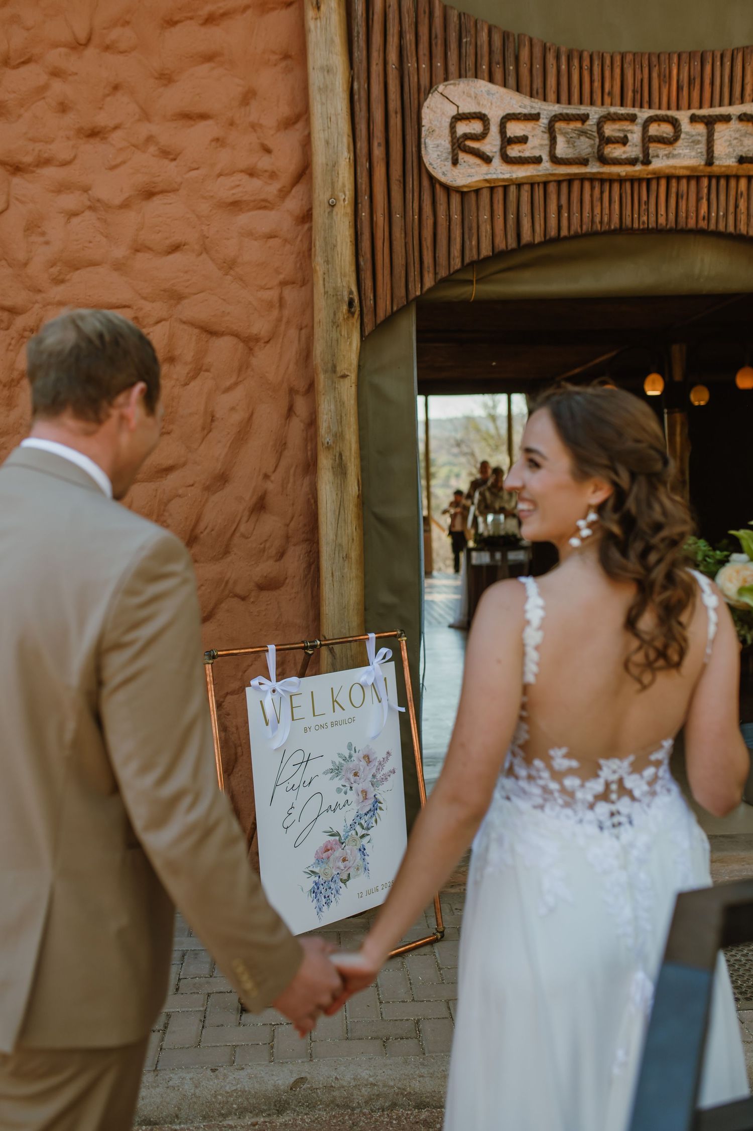 Wedding couple entering rustic reception area with welcome sign.