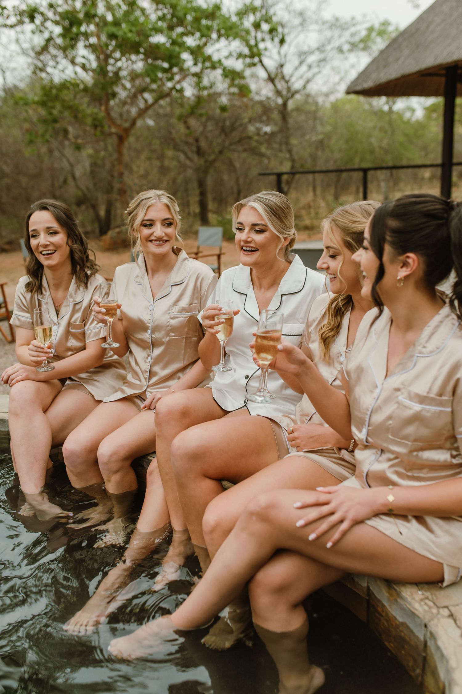 Friends in silk pajamas dangling their feet while sitting together on wooden deck railing.