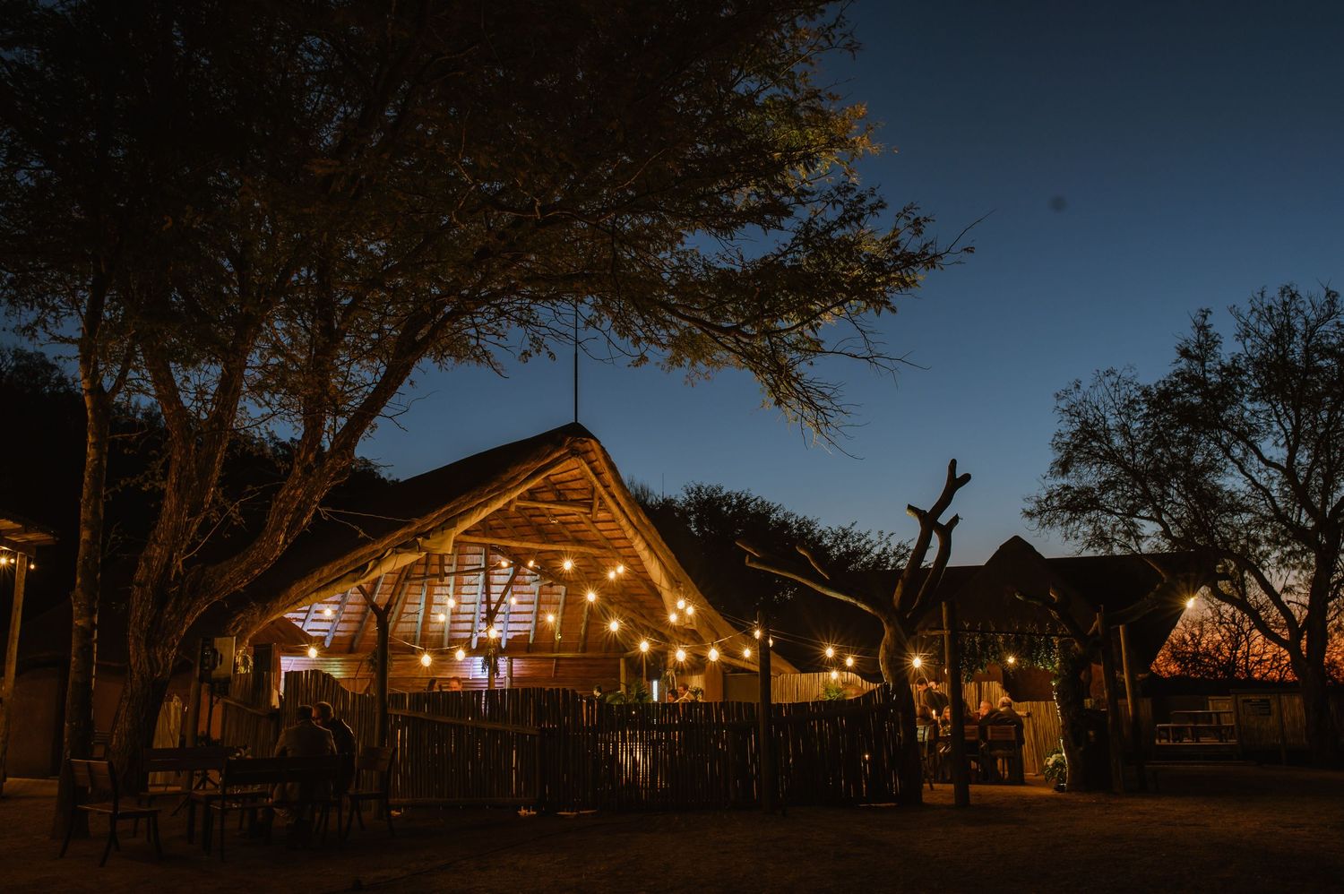 Panoramic view of a rustic wedding venue at dusk with string lights creating a magical atmosphere.