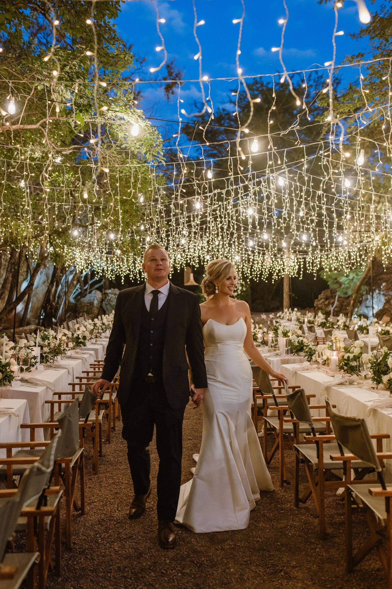 Wedding ceremony space decorated with cascading fairy lights and wooden chairs.