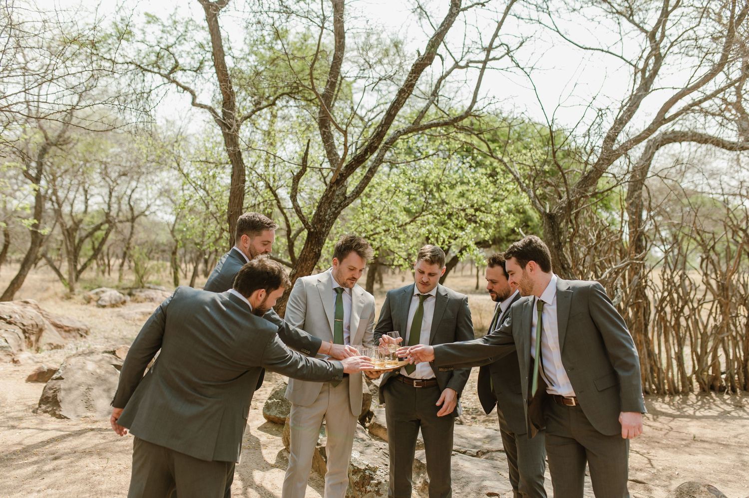 Wedding party gathered outdoors under trees in a natural setting.
